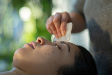 Obraz na płótnie Canvas Young woman receives facial rejuvenation with gua sha rose quartz in spa wellness center