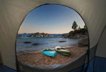 A view through a tent door of two paddle boards sitting on a beach.