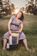 Country woman in retro scene washing clothes with a washboard outdoors at sunset