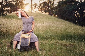 Pregnant woman wiping off sweat while washing clothes on a washboard in the summer.