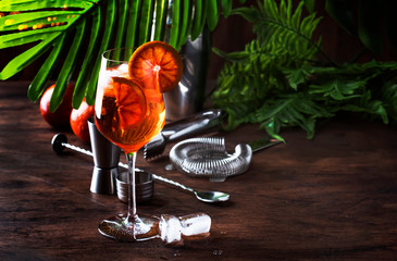 Aperol spritz cocktail in big wine glass with orange slices, summer cool fresh alcoholic cold beverage. Wooden bar counter background with tools, summer mood concept 
