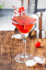 Classic alcoholic cocktail Manhattan with american bourbon, red vermouth, bitter, ice and cocktail cherry in glass, tools, gray bar counter background, copy space, selective focus