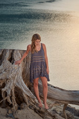 A young, barefoot woman in a boho style dress walking along the shorline of a mountain lake in Northern California while on vacation.