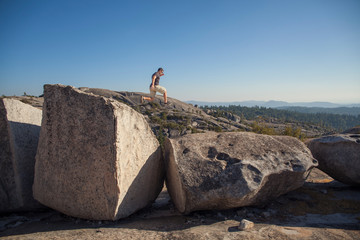Man in a remote outdoor location jumping from a large boulder.