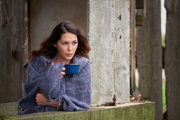 A farm girl blowing on her coffee while relaxing in the window of a small out building on a rural farm.