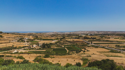 Fototapeta na wymiar Fields and plain under blue sky viewed from the city of Mdina, Malta