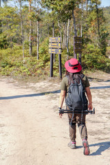 Fototapeta premium Woman traveler with backpack holding hat alone on dirt road at tropical forest. Female photographer outdoors in nature. travel holiday relaxation conceptt, space for text, atmospheric