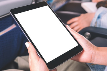Mockup image of a woman holding and looking at black tablet pc with blank white desktop screen while sitting in the cabin