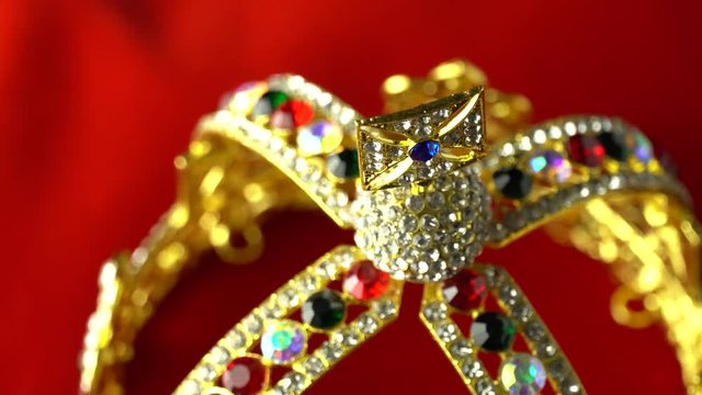 Extreme macro close up shifting focus at gold and jewel diamond King's crown on the red soft velvet royal ceremonial pillow. Slow rotation motion. 4k, uhd.