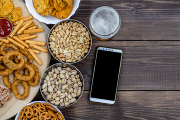Mix of snacks with beer and smartpnone on dark wooden background. Internet delivery concept. Top view. Empty space for text