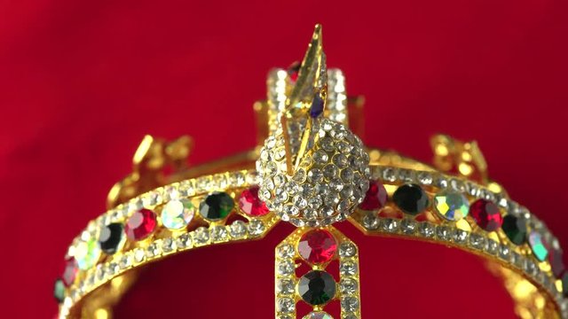 Gold diamond crown or decorative pageant accessory close up focus on the bottom frame. Slowly rotation on the red royal color surface. 4k, uhd.