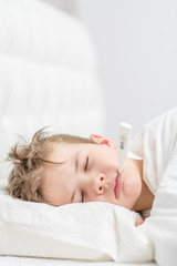 Sick boy sleep under blanket with thermometer in his mouth. Empty space for text