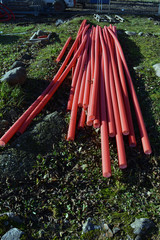 Stack red plastic electricity cable protection pipes on street lawn