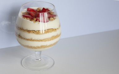 Dessert in a glass goblet. Layers laid biscuit crumbs and cream. Decorated with strawberry slices. With the addition of walnut. On a white background.