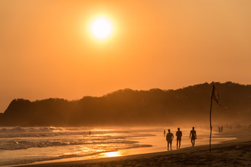 Fototapeta premium Magnifique couché de soleil sur la plage de Zipolite, Oaxaca, Mexique. Silhouettes de personnes marchant sur la plage en contre jour. 