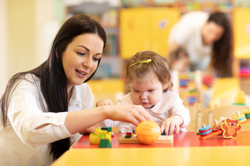 Nursery baby and teacher play with developmental toys in preschool