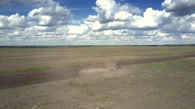 tremendous upper view endless gray field and old tractor harrows soil surrounded by dust cloud against cloudy sky