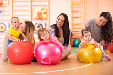 Fototapeta na wymiar Happy mothers and their babies on fitness ball in nursery. Gimnastics for kids on fitball.