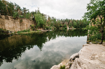 Fototapeta na wymiar Landscape of an old flooded industrial granite quarry filled with water. Lake on the background of rocks and fir trees. Canyon The nature of the autumn. Place for text and design.