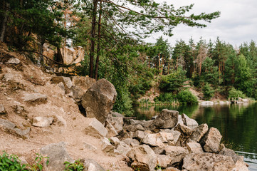 Rocks and stones fall in water. Lake on the background of rocks and fir trees. Canyon. Place for text and design. Landscape of an old flooded industrial granite quarry filled with water.