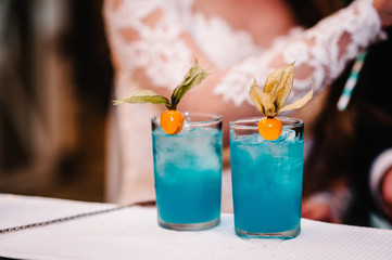 Fresh blue juice in the glass on the bar counter on background the bride and groom. Colorful cocktail at night club in wedding day.