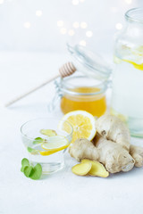 Healthy ginger drink in a cup. Ginger root, honey in a jar, lemon on a white table.