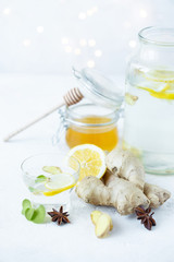 Healthy ginger drink in a cup. Ginger root, honey in a jar, lemon on a white table.