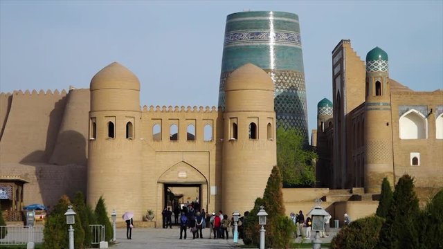 A wide shot of a mosaic temple complex in Xiva, Uzbekistan, with tiled tours, decorated walls, and people moving about outside