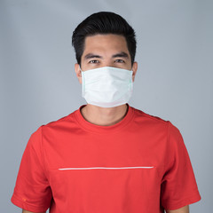 Close up sick young man handsome wearing medical mask and red shirt isolated on gray wall background. Concept of sick. Asia people.