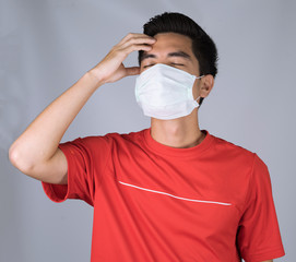 Sick young man handsome and headache wearing medical mask and red shirt isolated on gray wall background. Concept of headache. Asia people.