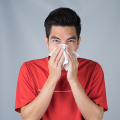 Sick young man handsome and sneeze wearing medical mask and red shirt isolated on gray wall background. Concept of sick. Asia people.