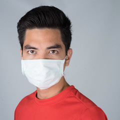 Sick young man handsome and sneeze wearing medical mask and red shirt isolated on gray wall background. Concept of sick. Asia people.