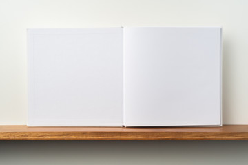 white square notebook on bookshelf and white wall