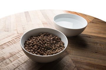 cat food dishes - two bowls of cat  dry food and water standing on a wooden table in front of white background