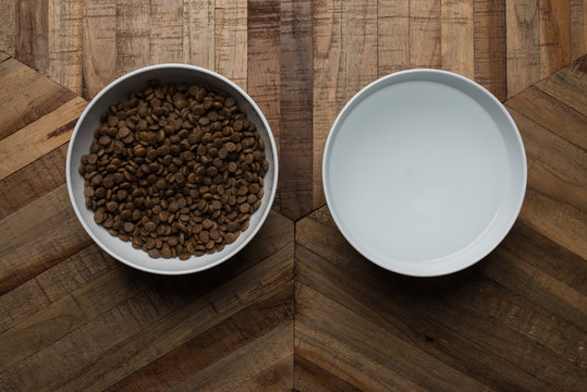 cat food dishes - top view of two white bowls of dry cat food and water standing on a wooden table © FurryFritz