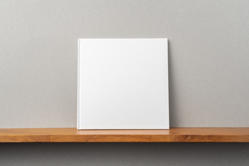 white square notebook on bookshelf and grey wall