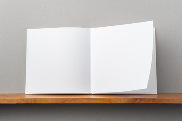 white square notebook on bookshelf and grey wall