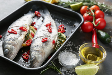 Fototapeta na wymiar Baking tray with fresh fish and ingredients on dark table