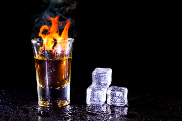 Hot alcoholic cocktail burning in shot glass with ice cubes.