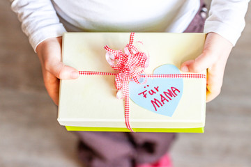 Little child holding gift box with ribbon and heart for her mum - Translation: for mum