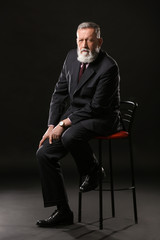 Obraz na płótnie Canvas Handsome mature businessman sitting on chair against dark background