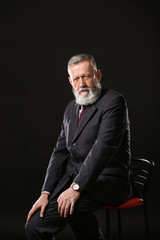Handsome mature businessman sitting on chair against dark background