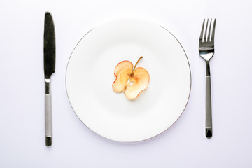 One slice of dried apple on white plate with cutlery on white background.