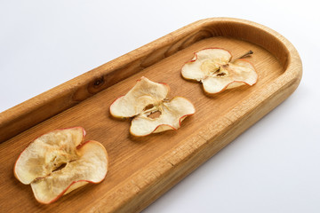 Close-up lying diagonally oblong wooden plate with apple chips on white background.