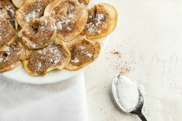 Close-up plate with apple chips sprinkled with powdered sugar and cinnamon and spoon on white background.