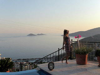young girl on the summer terrace at the seaside admires the sunset