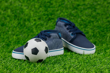 Concept encourage children to play sport, exercise for a healthy body, shoes of small baby shoes next to ball isolated on grass background.