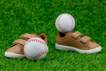 Concept encourage children to play sport, exercise for a healthy body, shoes of small baby shoes next to ball isolated on grass background.