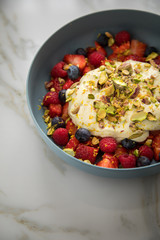 Beeren Obstsalat mit Erdbeeren, Himbeeren, Blaubeeren, Pistazien, Zitronen Zesten, Leinöl Kurkuma Quark Creme in blauer Schale als Frühstück auf Marmor Hintergrund