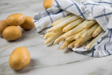 Roher, weißer Spargel in Tuch und Kartoffeln auf Marmor Hintergrund
